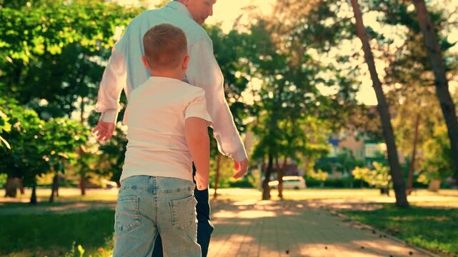 Child son plays with dad, running together in summer park. Family game. Cheerful little boy runs to catch up with dad outdoors. Carefree childhood. Child plays outside with dad. Dad fun with young son