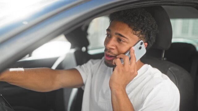 Man in car talking on smartphone with right hand to ear and left hand on steering wheel, parked at curb on street while smiling; happy connection.