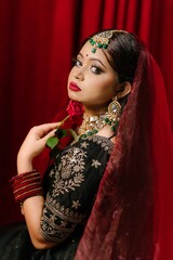 Side Profile Portrait of South Asian Bride Holding Red Rose near Chin in Red Sheer Veil © AHSANUL