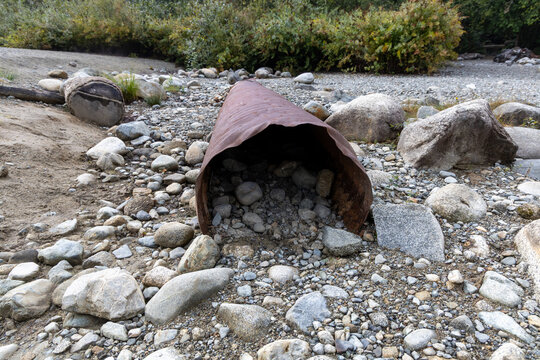 Rusted Metal Pipe in Rocky Dry Riverbed With Stones and Shrubs in BC, Canada