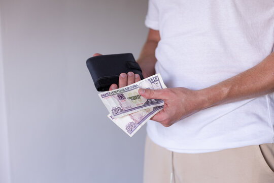  Man holding 100 Cuban peso banknote and wallet.