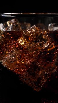 Pouring soda water into the glass. Closeup. Black background. Vertical footage
