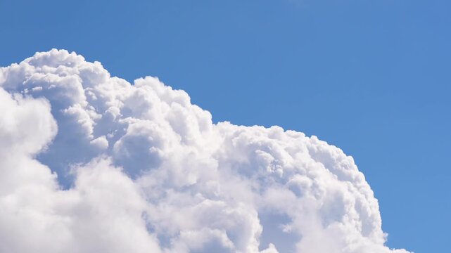Cinematic time lapse showing large white cumulus clouds rapidly changing shape and moving across a clear blue sky, representing weather dynamics, nature, atmosphere, climate and aerial background conc