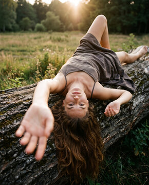 Dreamy woman lying backward on fallen tree trunk reaching hand toward camera outdoors