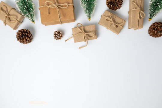 Kraft paper presents, pinecones and small bottlebrush trees form a top border against a clean white background with copy space.