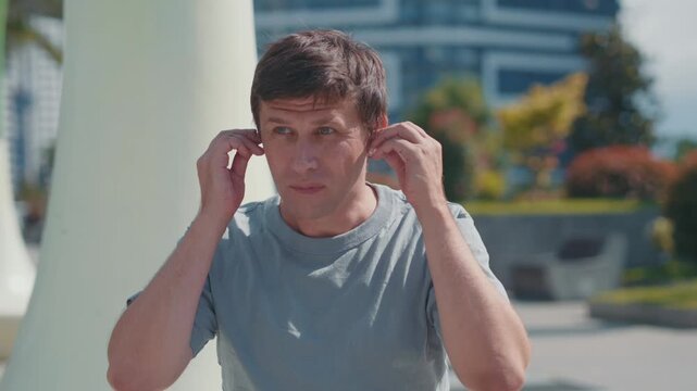 Man inserting wireless earbuds and tapping to activate noise cancellation, finding quiet and relaxation amid city noise pollution.