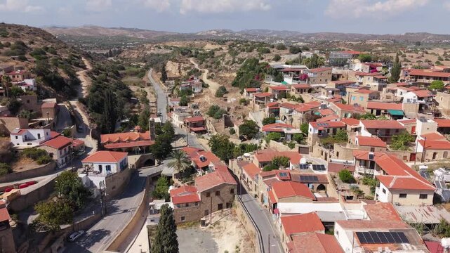 Panoramic view of Tochni village in Cyprus with traditional stone houses, red tiled roofs, cypress trees, winding roads and dry Mediterranean hills