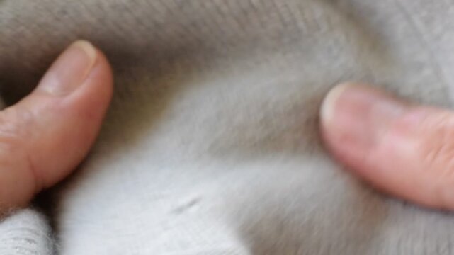 Closeup static shot showing hand holding and manipulating light gray sweater to reveal small moth holes and fabric damage in the knit material. 