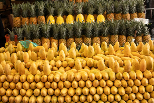 A colorful display of fresh pineapples and ripe mangoes arranged at a tropical fruit market