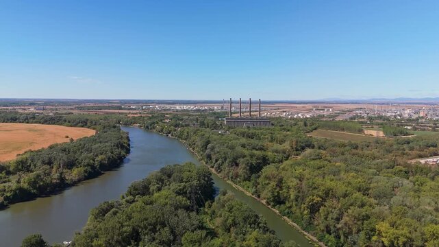 Tiszapalkonya, Hungary decommissioned thermal power plant with cooling towers and smokestacks beside the Tisza River, surrounded by forest and fields in summer, filmed by drone.