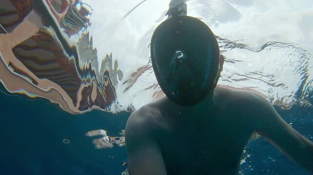 A man treading water while snorkling with a leisure boat visible through the sea ripples above