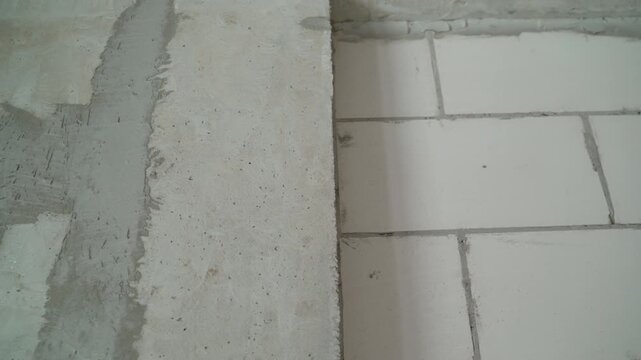 Close up pan shot reveals details of wall construction. Unfinished concrete surface transitions to new wall made of white aerated concrete blocks. Interior renovation or building process concept