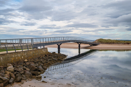 Modern pedestrian bridge crossing over the River Lossie at low tide near the scenic coastal town of Lossiemouth in the region of Moray, Scotland