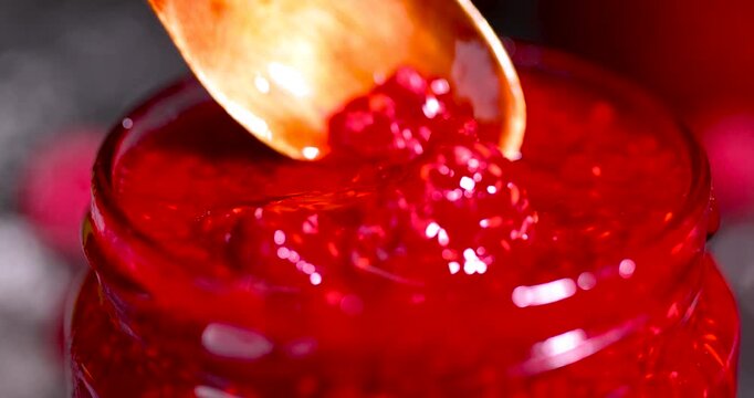 grated raspberries in a glass jar with a wooden spoon, an open jar of grated raspberries stands on a black stone table surrounded by berries