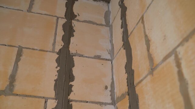 Close up video of a newly constructed wall corner. The wall is made of beige aerated concrete blocks joined with wet, gray mortar. Scene from a construction site showing masonry details