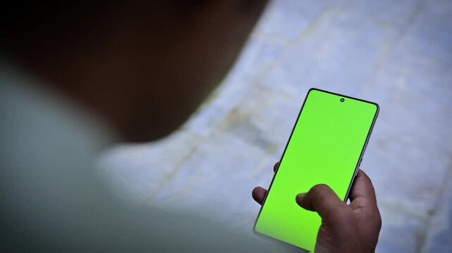 Person holding smartphone outdoors with green screen chroma key, side view of male hand using mobile phone display mockup for screen replacement and application presentation
