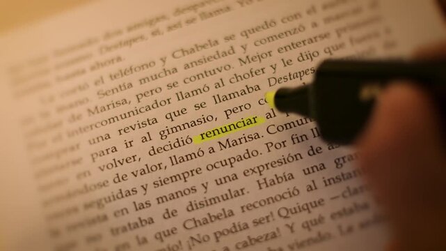 4K slow-motion close-up of a hand using a yellow marker to highlight the word 'renunciar' on a moody book page.