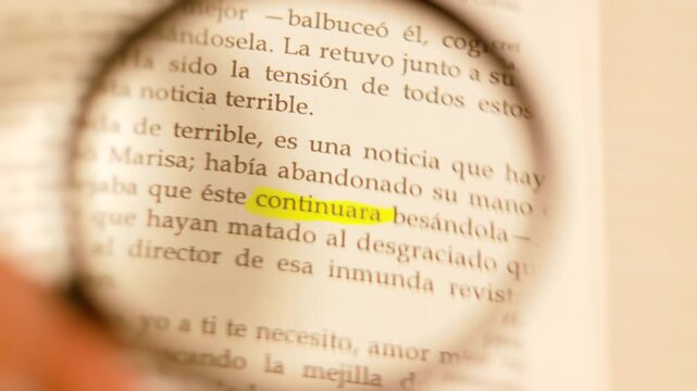 Cinematic 4K slow-motion close-up of a magnifying glass magnifying the highlighted word 'continuara' in a Spanish book.
