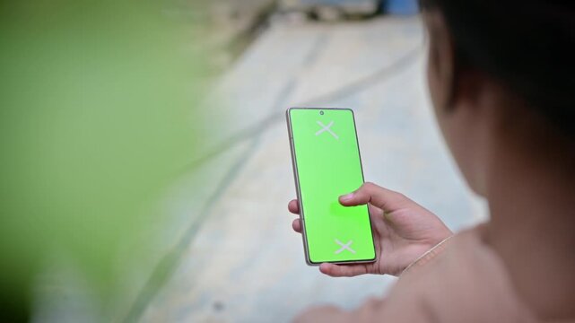 Woman holding smartphone with green screen display from side angle, female hands operating mobile phone chroma key mockup for website preview and video mockup replacement