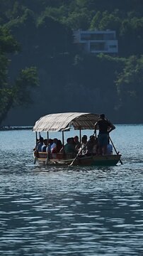 Ljubljana, Slovenia, 26 August 2025: Bled lake. Slow motion. Wooden boat floats gently on a deep blue lake. Tourists under a straw roof relax and smile. Lush green trees surround the water's edge. Dis