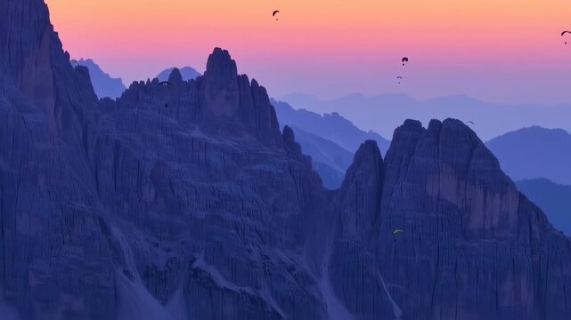 Silhouette of mountains against a colorful sunset, featuring paragliders in the sky