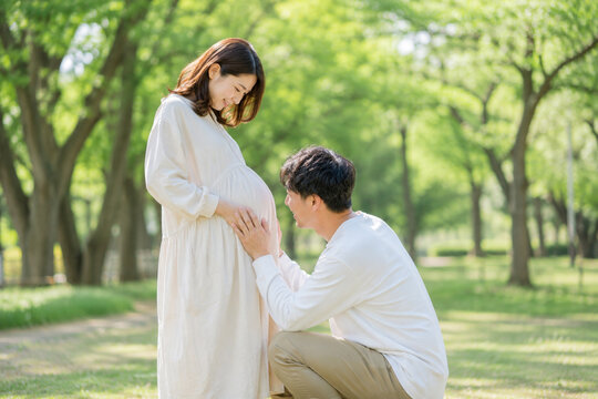 公園で夫が妊婦のお腹にやさしくキスするマタニティ風景