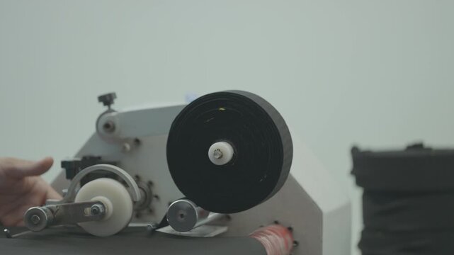 Close up of industrial tape applicator machine spool and roller mechanism operating in factory packaging line