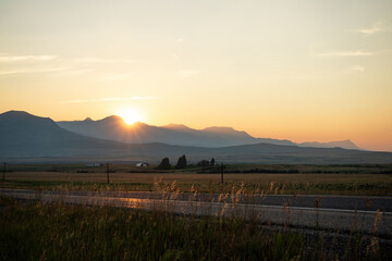 A stunning sunset illuminates a serene mountain landscape and empty country road, creating a peaceful mood perfect for travel and nature themes © Viks