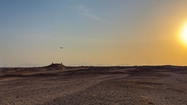 Airplane flying over a sandy desert landscape at sunset