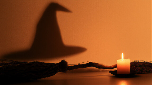 Witch hat shadow cast on wall beside burning candle and old broomstick. Spooky halloween still life in warm candlelight glow.
