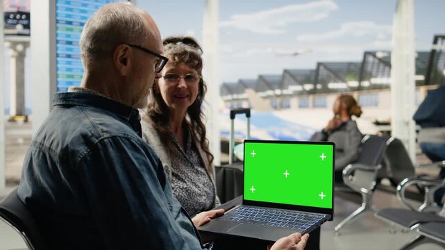 Green screen on a laptop is held by a senior traveler in an airport lounge while waiting at the gate before departure as the elderly man plans itinerary and travel details using the mockup display.