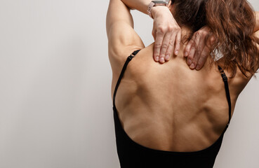 Fototapeta premium Athletic woman herself hands massaging her upper back, neck, trapezius muscles in pain, tension, soreness, recovery, posture, wellness. Selfcare after exercise with studio light copy space. Rear view