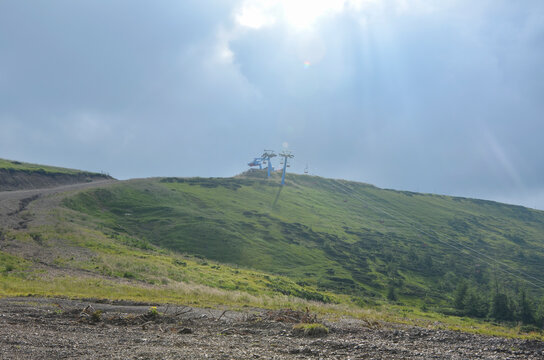 Chairlift station sits atop a green mountain ridge under dramatic sunlight breaking through dark clouds. Dragobrat, Carpathian Mountains, Ukraine