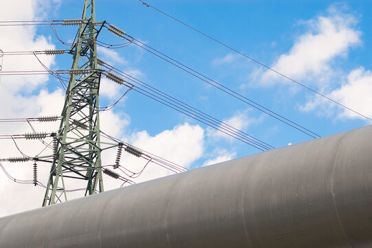 A close-up of a pipeline and a power transmission tower against a blue sky