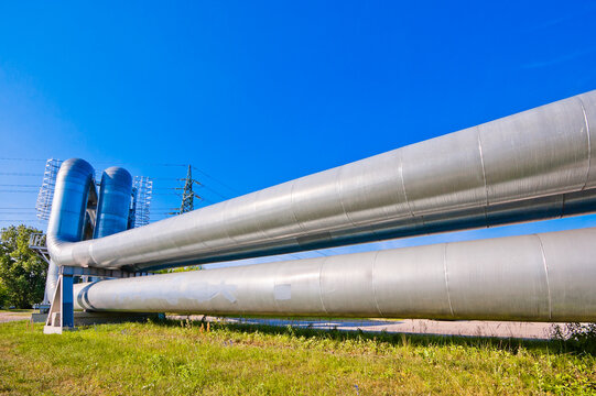 A close-up of a pipeline, with a blue sky and a power transmission tower in the background
