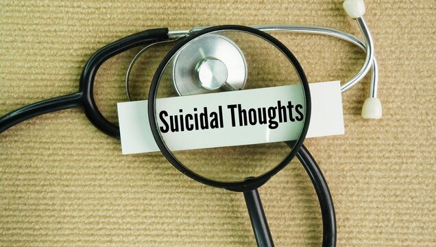 A magnifying glass, a stethoscope and a paper tag with the words Suicidal thoughts. thoughts, ideas, or fantasies about wanting to end your life, wishing you were dead, or feeling that others would be