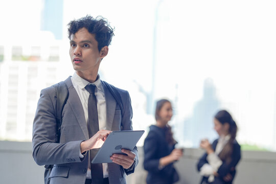 An Asian office worker in formal wear taking a moment to reflect with a tablet on a skywalk above the business district, showing confidence and focus in a contemporary workplace