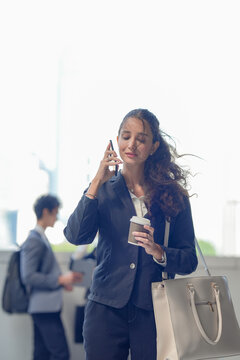 A young female executive in a formal suit smiling at a message on a smartphone with coffee on a skywalk above the business district, conveying focus, drive and everyday professionalism