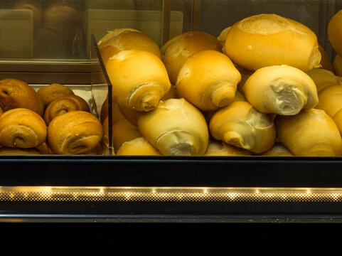 Assorted fresh breads and rolls displayed in a warmly lit bakery glass case
