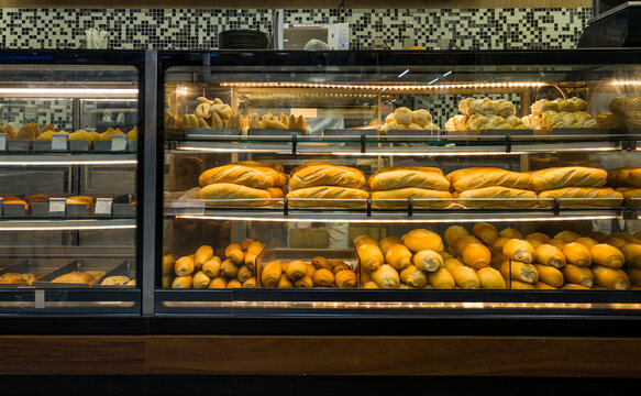 Assorted fresh breads and rolls displayed in a warmly lit bakery glass case