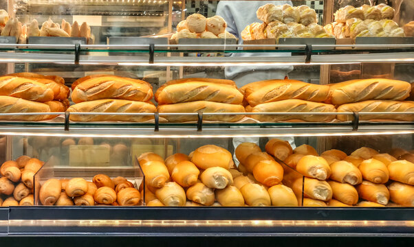 Assorted fresh breads and rolls displayed in a warmly lit bakery glass case