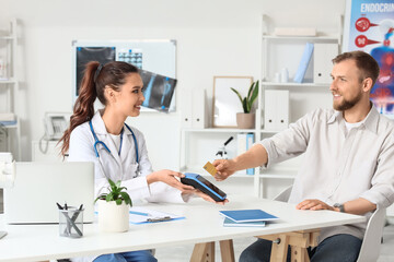 Male patient with credit card and doctor paying via terminal in clinic