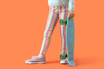 Legs of little girl with skateboard on orange background, closeup © Pixel-Shot