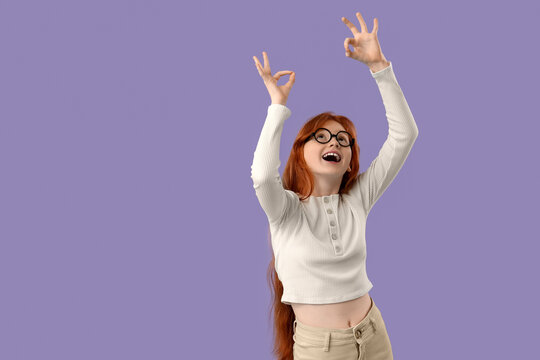 Teenage redhead girl showing OK gestures on lilac background