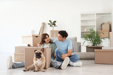 Happy young couple with French bulldog and cardboard box in rented apartment on moving day