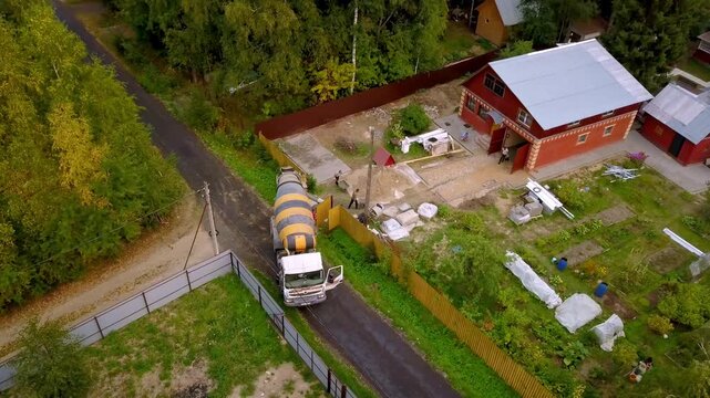 Aerial drone shot of concrete mixer truck delivering cement to a private construction site in a rural village