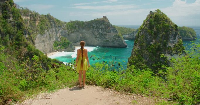 Woman opens arms wide standing on high cliff above Diamond Beach in Nusa Penida island Bali