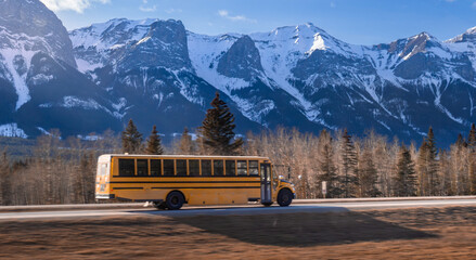 Yellow school bus driving on road toward snow capped mountain peaks under blue sky in Canadian Rockies © Vadim Rodnev