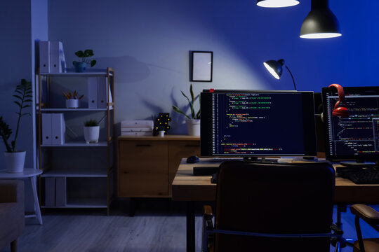 Programmers desk with computer monitors and glowing lamps in dark office at night