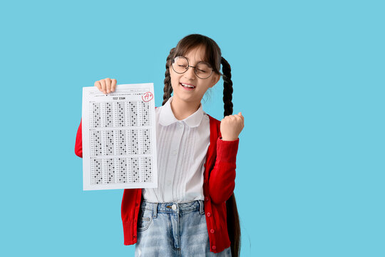 Happy schoolgirl holding good results of school test on blue background